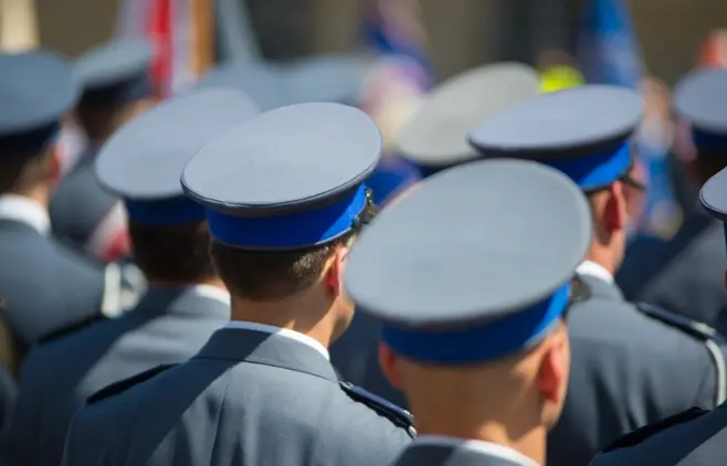 Grupa umundurowanych osób – policjantów widzianych od tyłu.